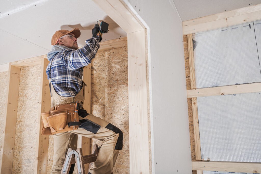 General Construction Contractor Attaching Drywall Using Cordless Drill Driver. Caucasian Remodeling Worker in His 40s.